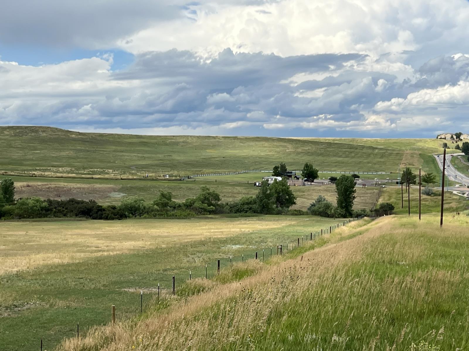 An image of the span of Open Space at Coalton Trailhead off McCaslin Rd, shows the depiction of short grass versus untouched native grass. There is a trailer in the background near the trailhead and the sky is full of clouds.