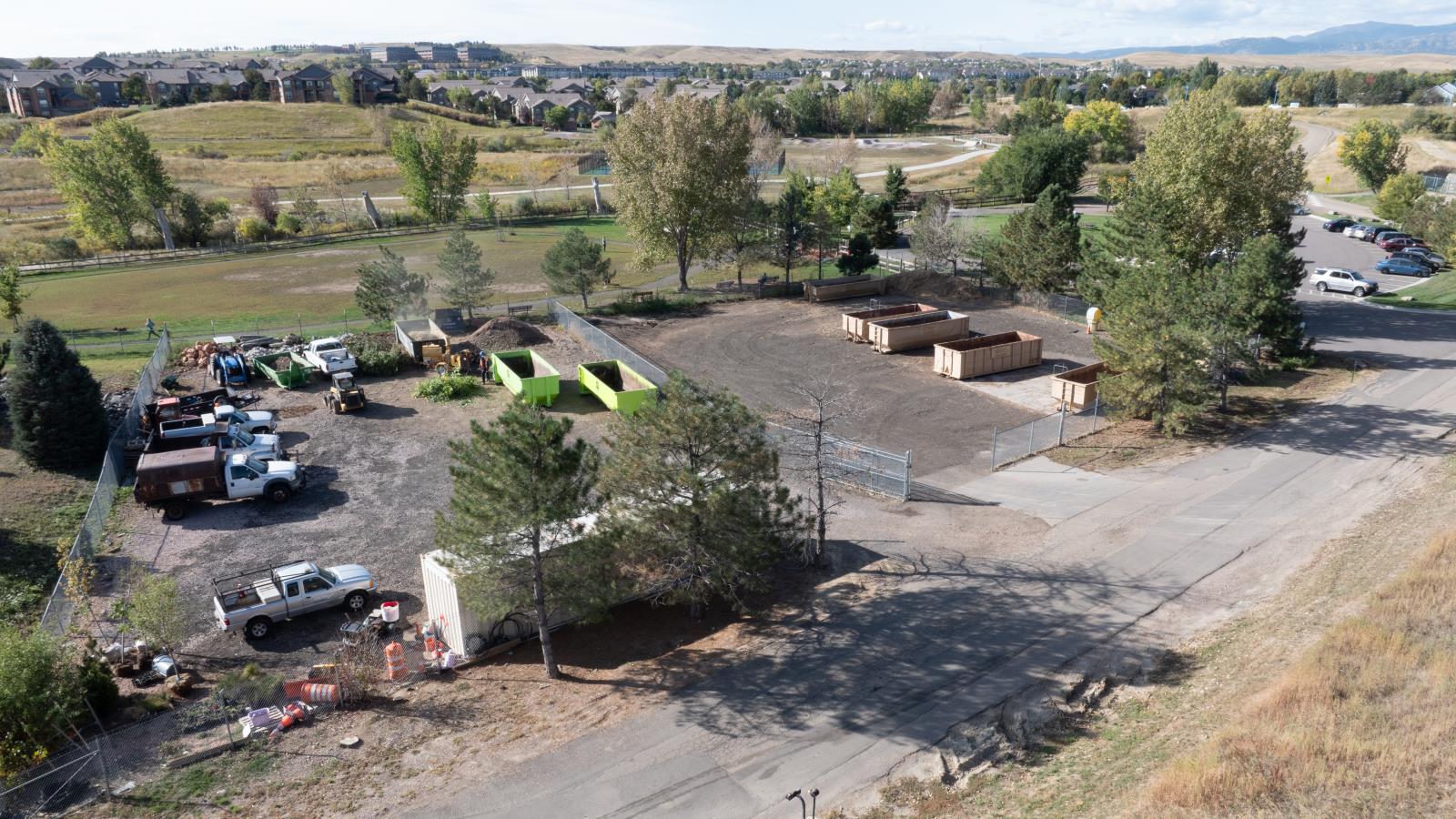 Arial photo of the Yard Waste Site, which is a mostly empty lot with public works vehicals parked on it and large dumpsters for waste disposal.