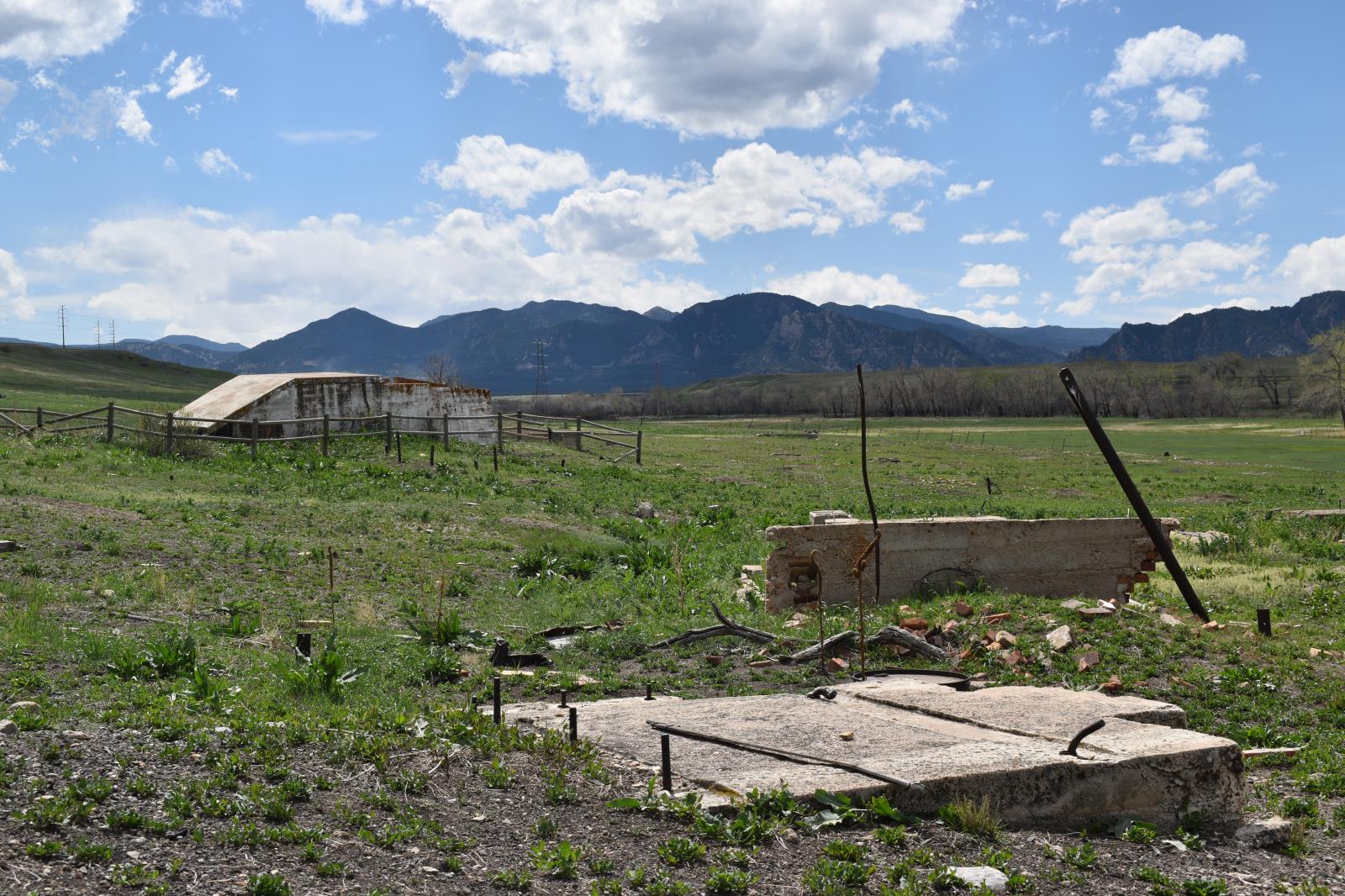 View of Boulder County Open Space and visible concrete building foundation remnants. Partly cloudy sky and mountains off in distance.