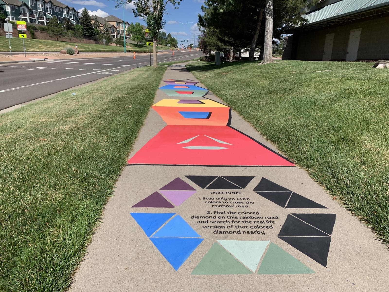 Geometric patterns in black, purples, red painted on a sidewalk near the Community Center