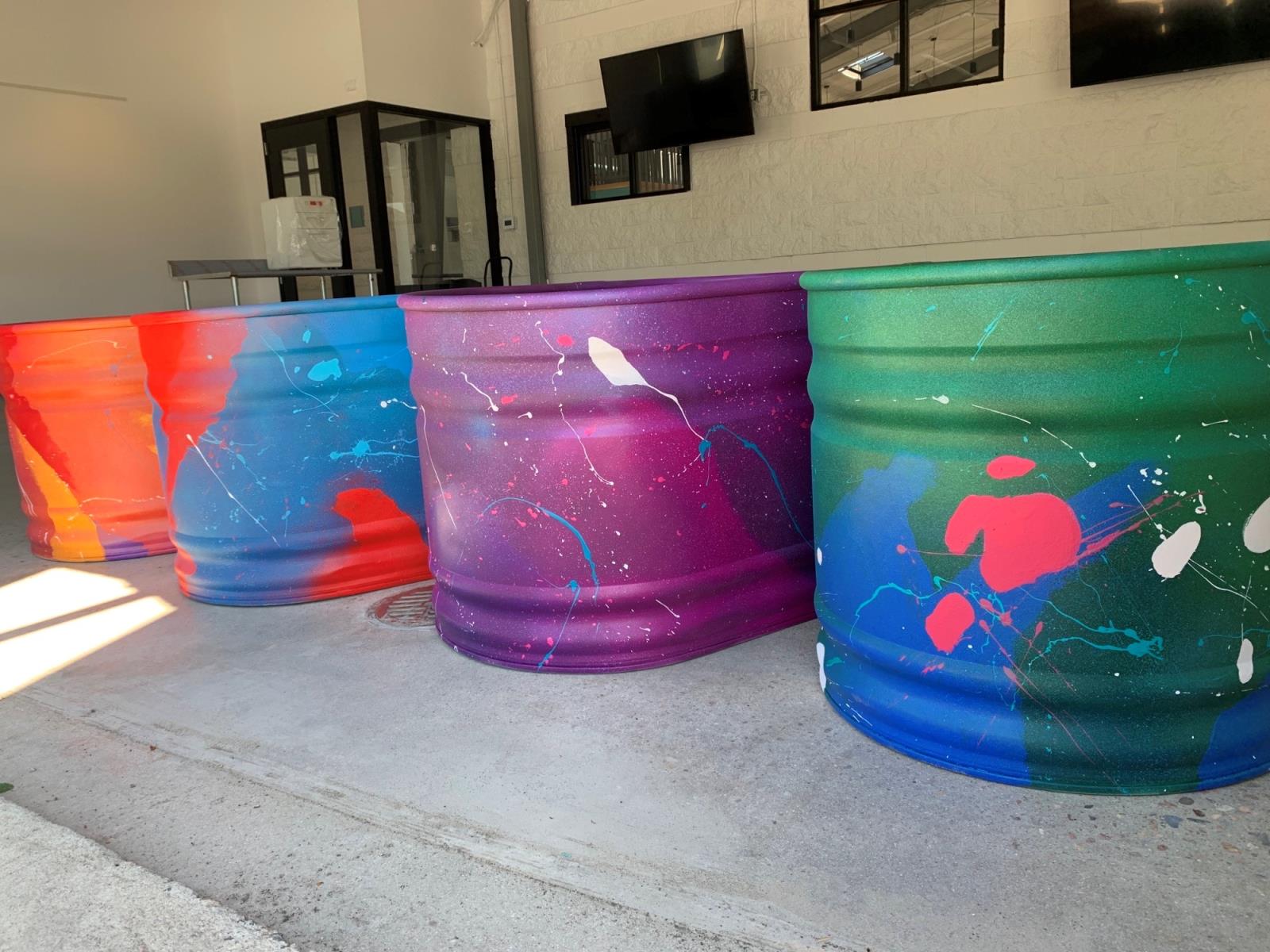 Four large steel stock tanks painted in bright colors and abstract patterns.