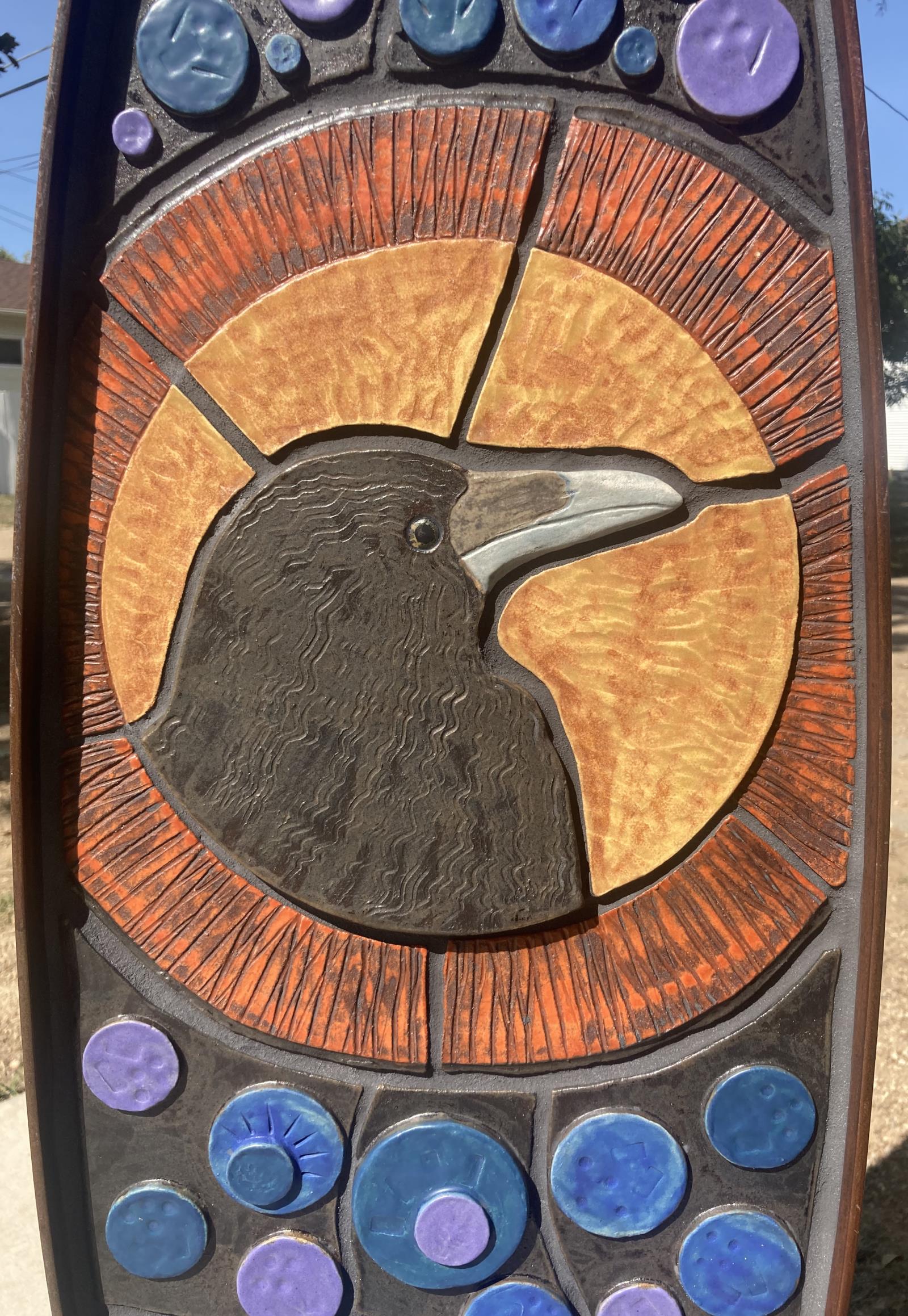 Shaped ceramic pieces form a raven in black with round gold backdrop and encircling orange ring