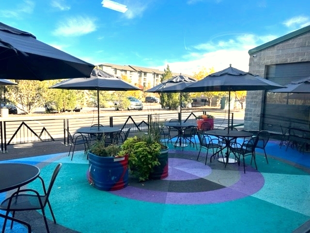 View of the patio at the Superior Community Center with a colorful ground mural beneath the patio tables and chairs. The mural is painted in blues and purples of geometric patterns of mostly concentric circles.