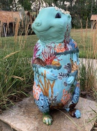 A four-foot tall 3-D fiberglass prairie dog statue painted light blue with plant and coral life painted sporadically around it's body to replicate the ocean. The prairie dog is wearing a crown made of real seashells.