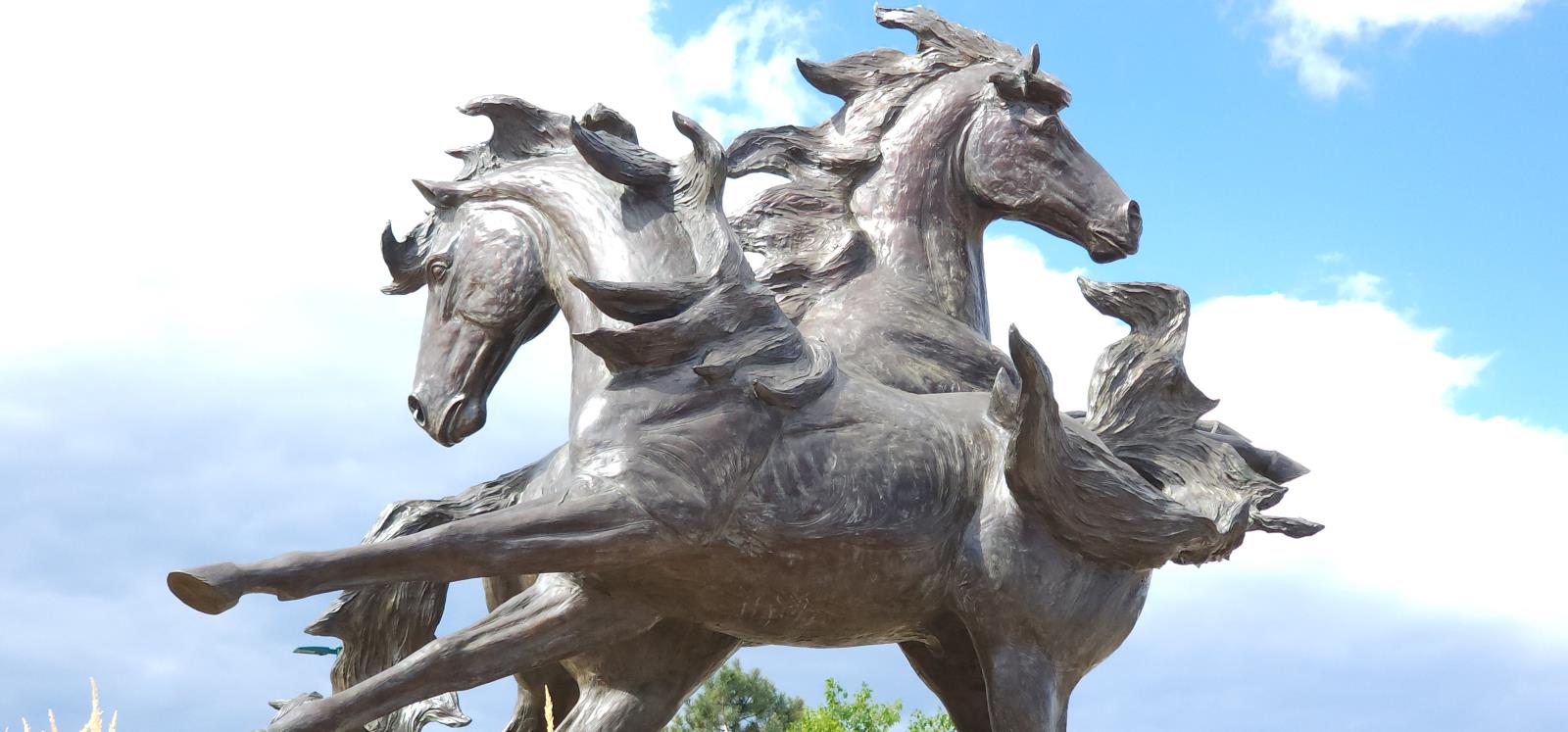 A bronze sculpture of three intertwined, life-size horses running in the wind. Their manes are blowing and front legs extended forward.