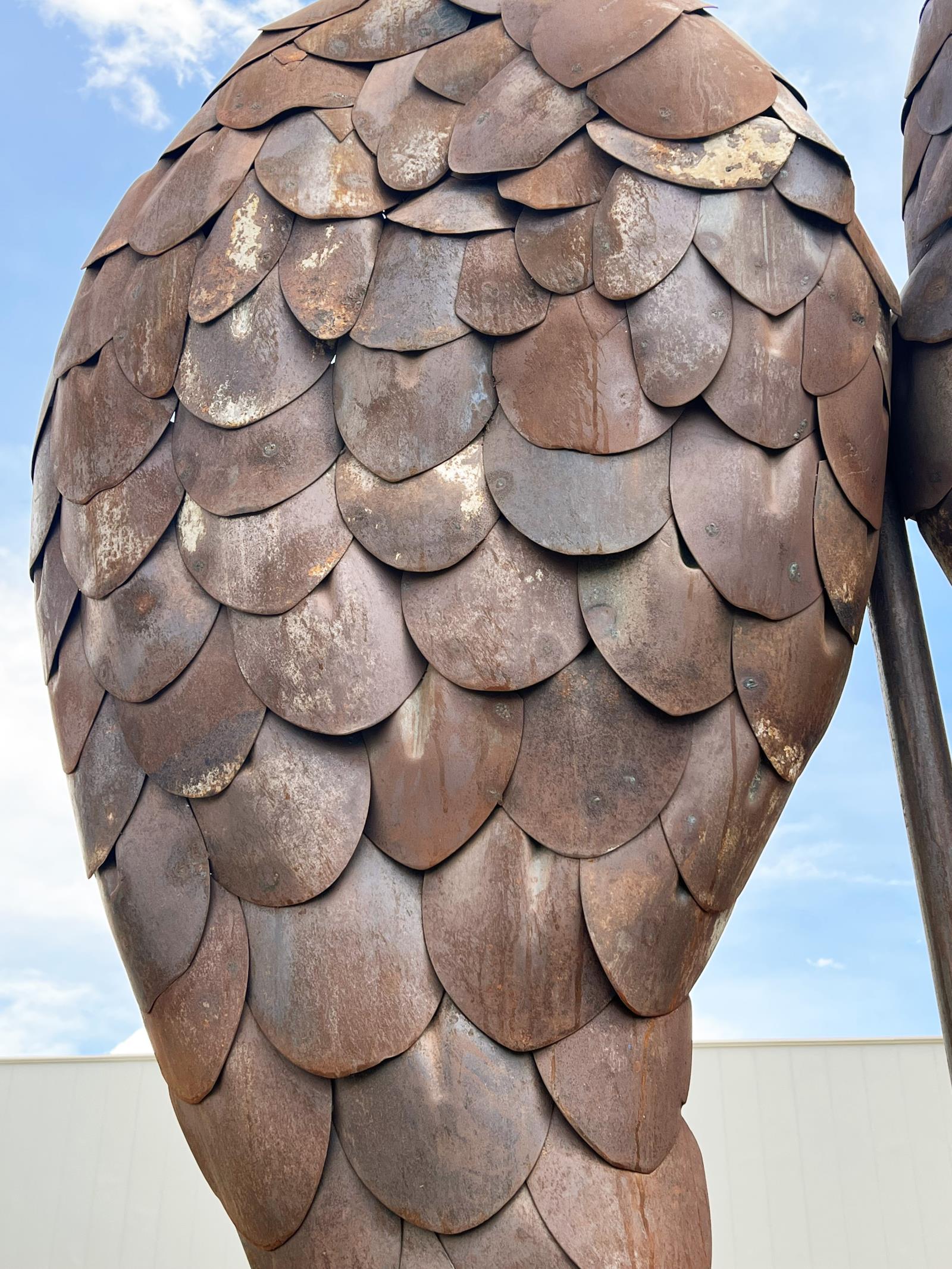 A cropped left-side image of an angel wing made of recycled shovel blades. The blades are rusted in many tones of red, brown and gray.