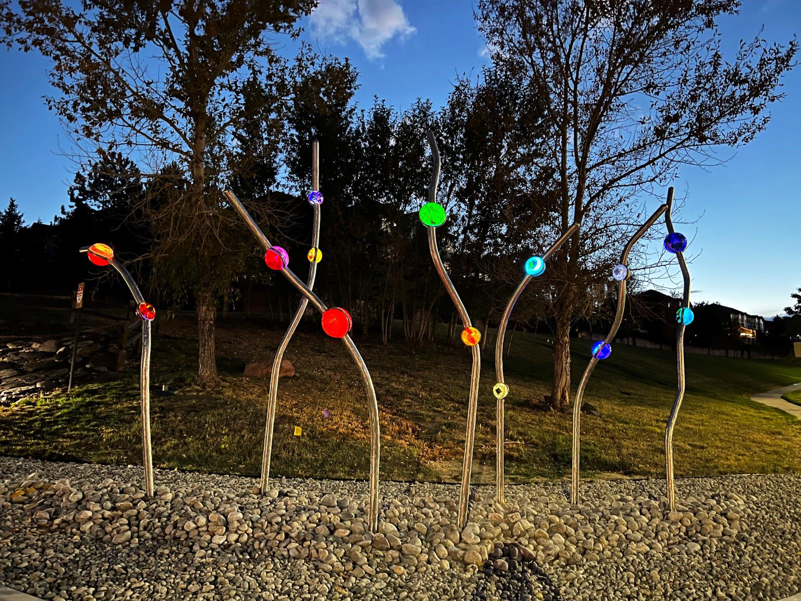 Nighttime view of seven stainless steel poles in whimsical shapes with illuminated blown glass orbs attached