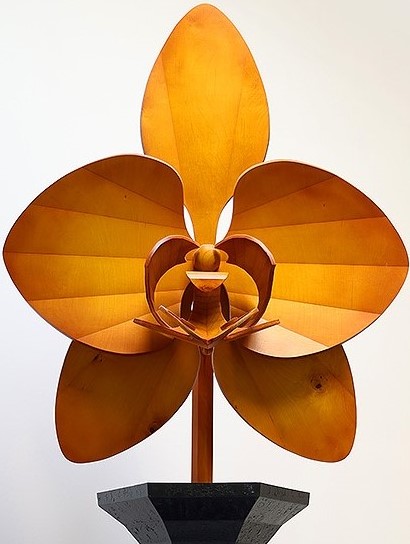 Close up of a yellow-ish brown stained wood orchid poking out from the top rim of a black wooden vase.