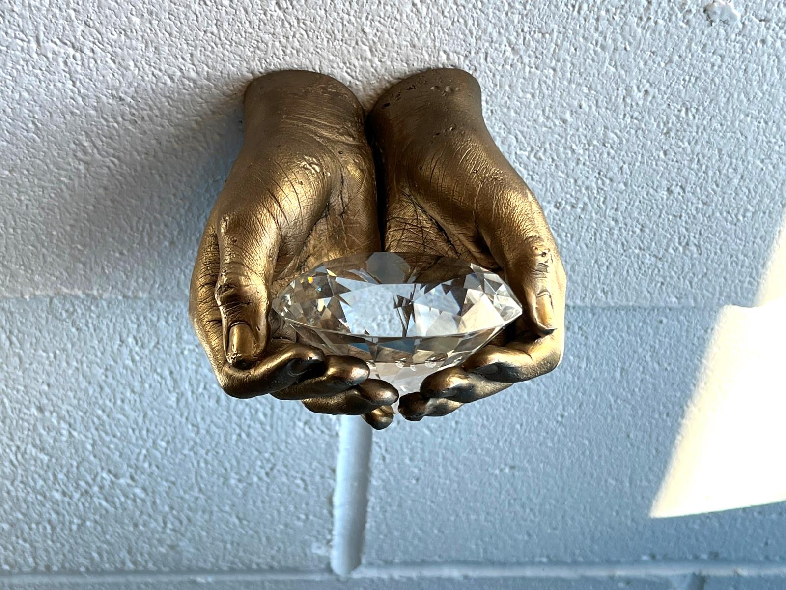 Bronze cast cupped hands holding a large clear diamond shaped gem