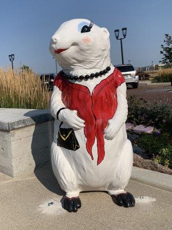 A four-foot tall 3-D fiberglass prairie dog statue painted white with a red shawl, black purse, black shoes, red lips, blue eyeshadow and long eyelashes. A real beaded necklace is around her neck.