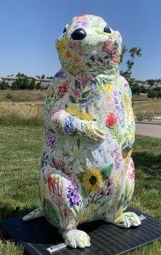 A four-foot tall 3-D fiberglass prairie dog painted white statue covered completely in a variety of delicately painted wildflowers in a range of different colors.