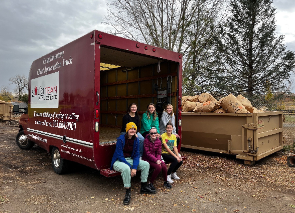 Girl Scout troop sitting in front of dumpster packed with leaves.